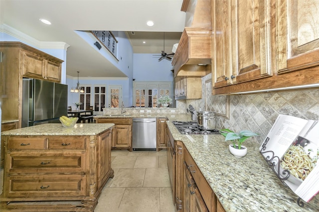 kitchen featuring ceiling fan, appliances with stainless steel finishes, a kitchen island, and light stone counters