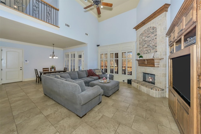 living room featuring ceiling fan with notable chandelier, a stone fireplace, ornamental molding, and a towering ceiling