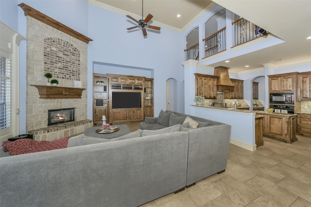 living room featuring a fireplace, a towering ceiling, crown molding, and ceiling fan