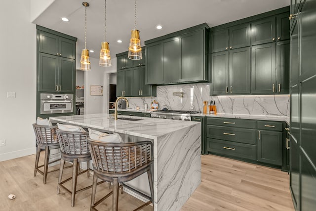 kitchen featuring sink, oven, green cabinetry, light stone countertops, and a kitchen island with sink