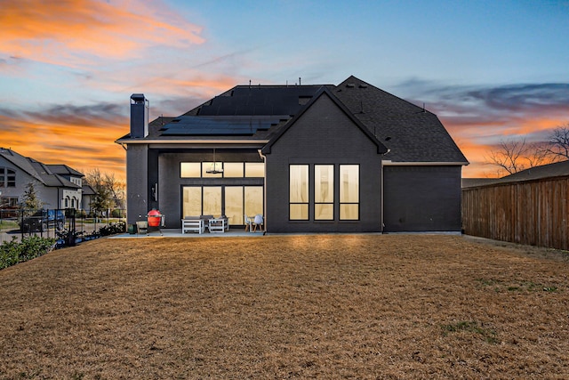 back house at dusk featuring a patio area, solar panels, and a yard