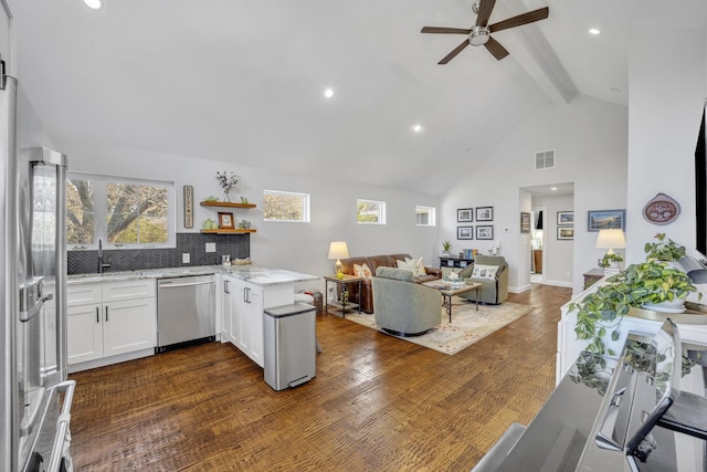 kitchen with kitchen peninsula, stainless steel appliances, beamed ceiling, sink, and white cabinets