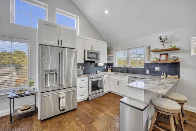 kitchen with a kitchen bar, appliances with stainless steel finishes, white cabinetry, dark hardwood / wood-style floors, and light stone countertops