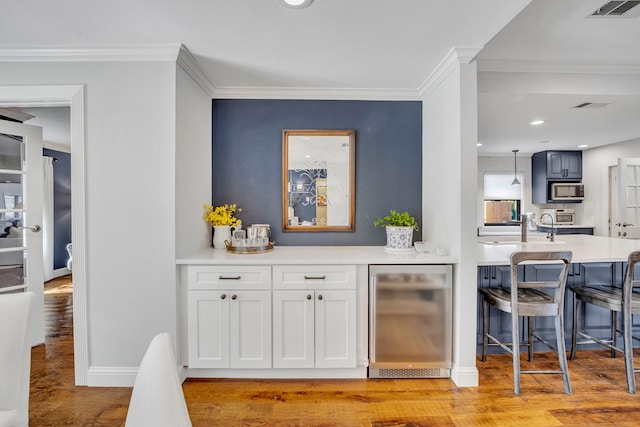 bar with white cabinetry, ornamental molding, sink, and light hardwood / wood-style flooring