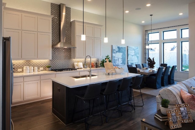 kitchen featuring a center island with sink, stainless steel appliances, decorative light fixtures, sink, and wall chimney exhaust hood