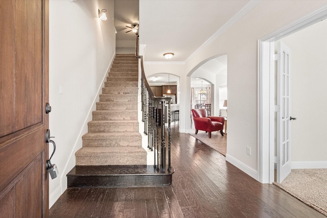 staircase with crown molding, wood-type flooring, and an inviting chandelier