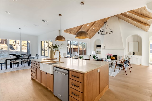 kitchen featuring dishwasher, an island with sink, light countertops, pendant lighting, and a sink