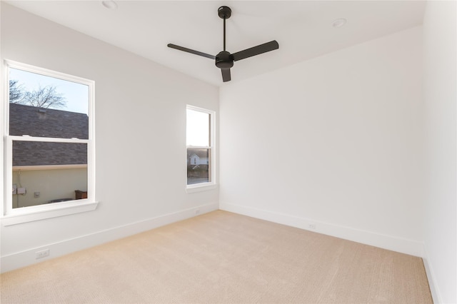 spare room featuring light carpet, a ceiling fan, and baseboards