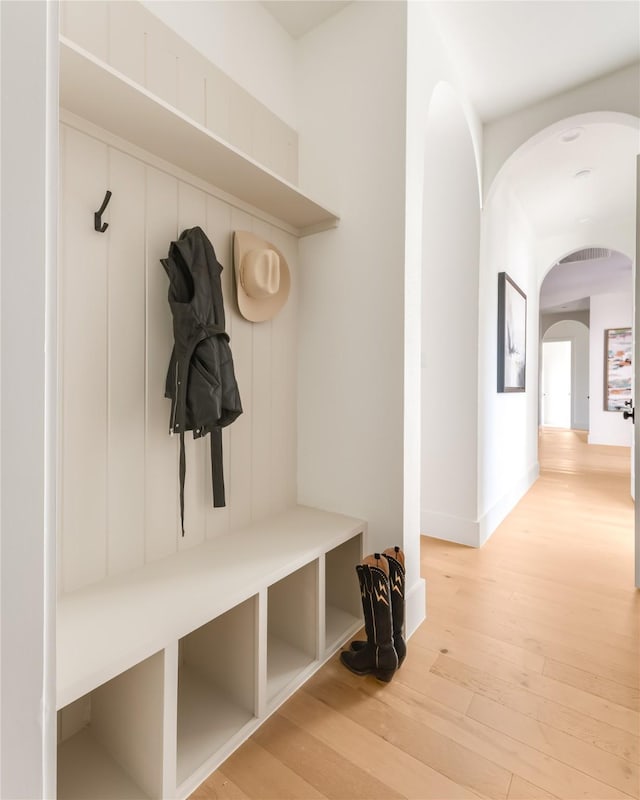 mudroom featuring light wood-style floors, arched walkways, and baseboards