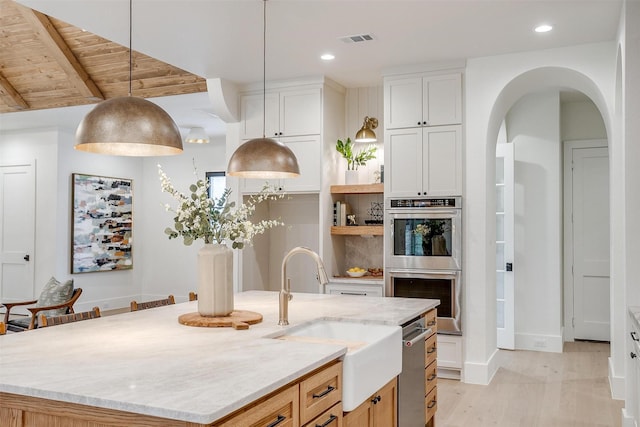 kitchen with double oven, light stone counters, a kitchen island with sink, visible vents, and white cabinetry