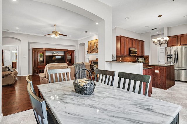 tiled dining room featuring crown molding, ceiling fan with notable chandelier, and a fireplace