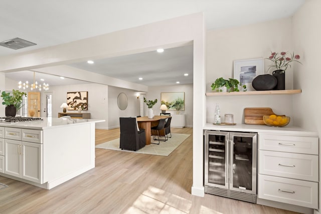 bar featuring beverage cooler, stainless steel gas cooktop, visible vents, hanging light fixtures, and light wood finished floors