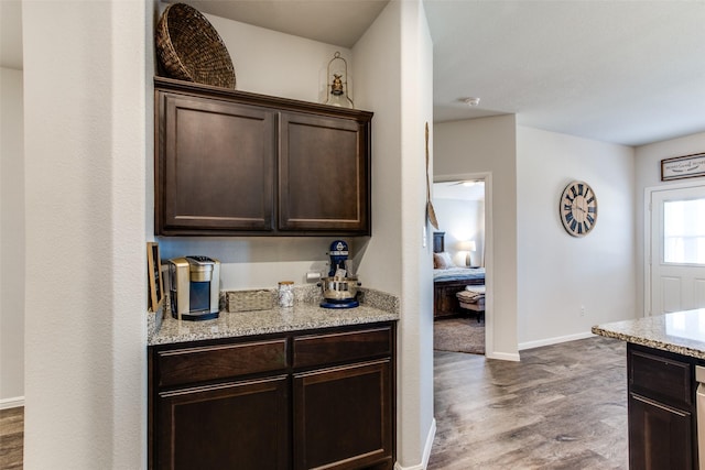 kitchen featuring dark brown cabinetry, wood-type flooring, and light stone counters