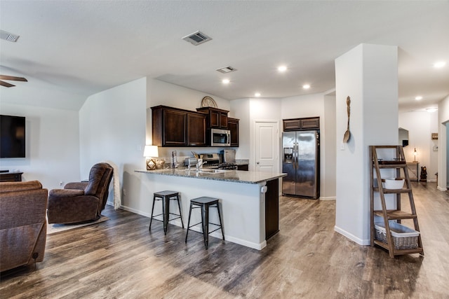 kitchen featuring kitchen peninsula, hardwood / wood-style flooring, dark brown cabinets, appliances with stainless steel finishes, and stone countertops