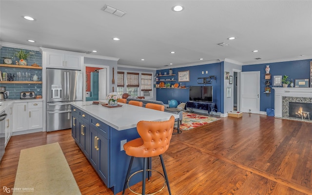 kitchen with blue cabinets, open floor plan, stainless steel fridge, white cabinets, and a tile fireplace