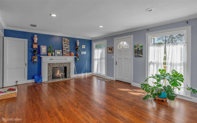 unfurnished living room with a tiled fireplace, crown molding, wood finished floors, and visible vents