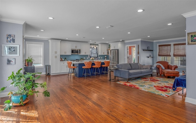 living area with visible vents, crown molding, baseboards, dark wood-type flooring, and recessed lighting