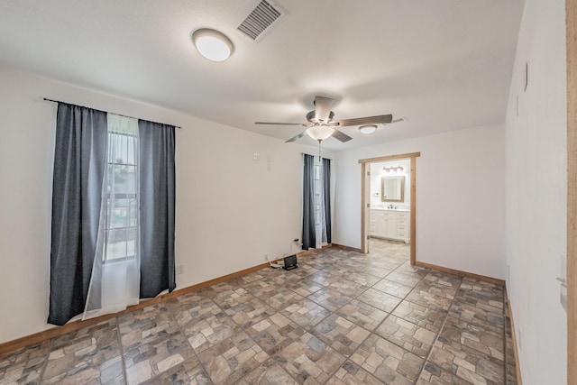 unfurnished room with stone finish floor, baseboards, visible vents, and a ceiling fan