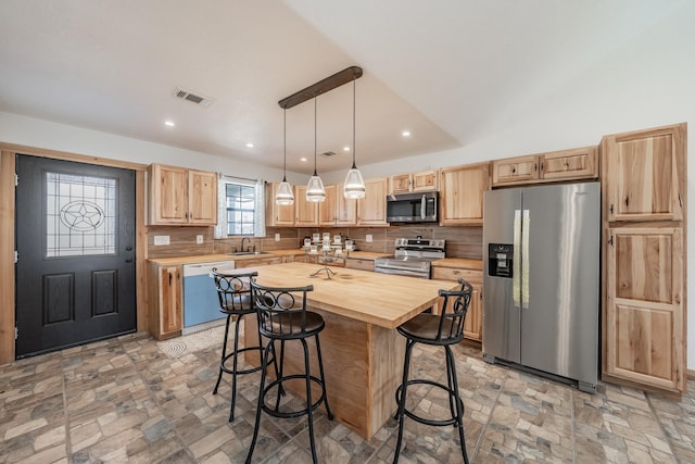 kitchen with a center island, pendant lighting, appliances with stainless steel finishes, stone finish floor, and a sink