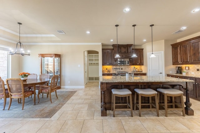 kitchen with hanging light fixtures, a large island, light stone counters, a raised ceiling, and sink