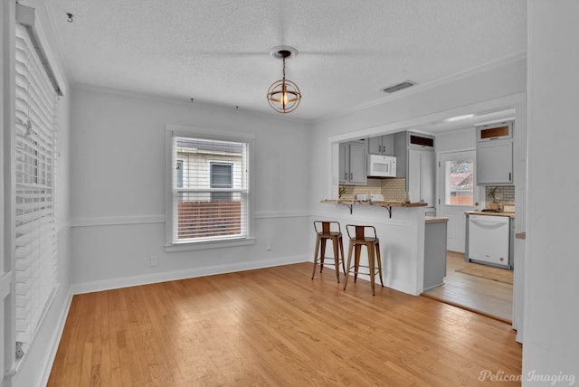 kitchen featuring visible vents, backsplash, a breakfast bar area, light wood-type flooring, and white appliances