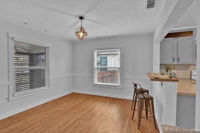 dining room with light wood finished floors, visible vents, crown molding, baseboards, and a textured ceiling