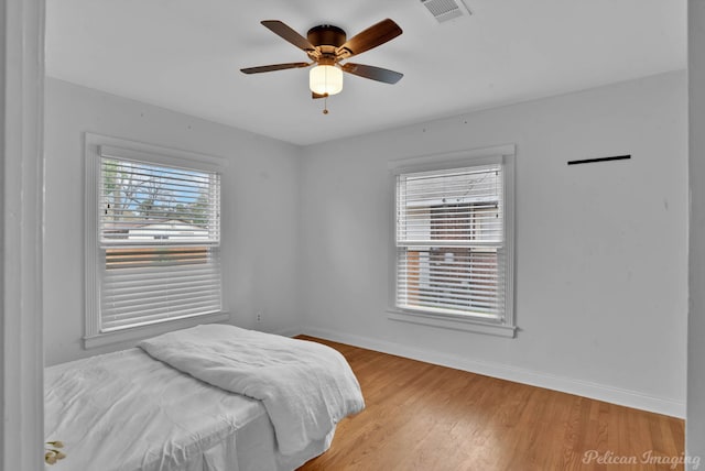 bedroom with visible vents, baseboards, wood finished floors, and a ceiling fan