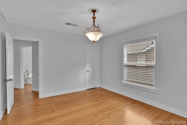 spare room with light wood finished floors, visible vents, a textured ceiling, and baseboards