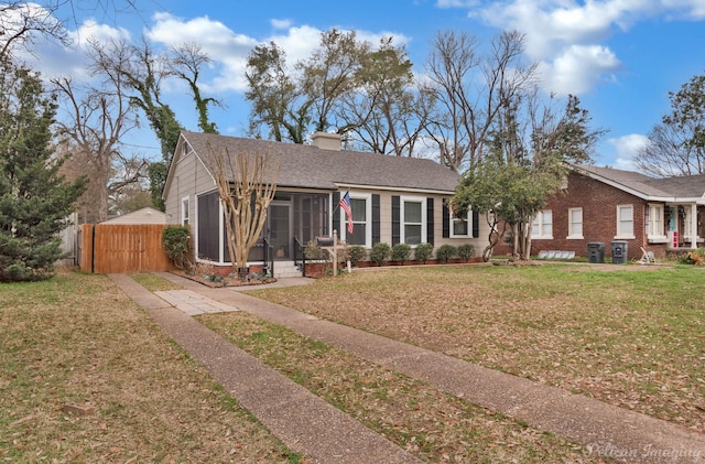 view of front of home featuring a front lawn, fence, roof with shingles, a chimney, and a sunroom