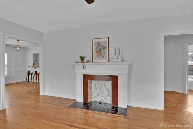 unfurnished living room featuring a fireplace, a textured ceiling, baseboards, and wood finished floors