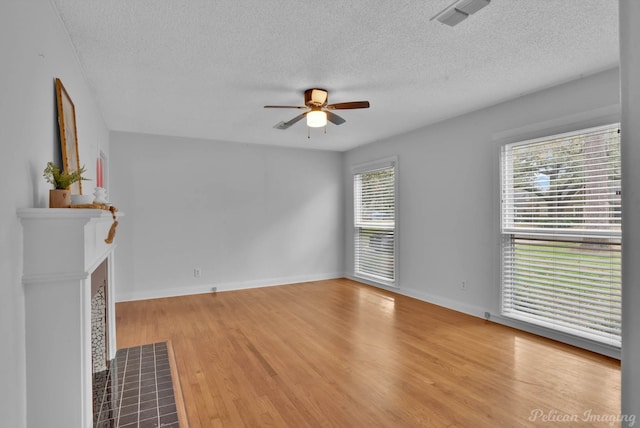 unfurnished living room featuring wood finished floors, baseboards, visible vents, ceiling fan, and a tile fireplace