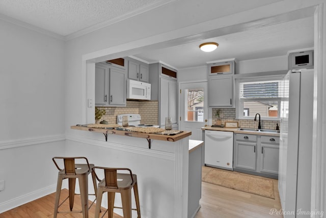 kitchen featuring white appliances, light wood finished floors, a sink, crown molding, and a kitchen breakfast bar