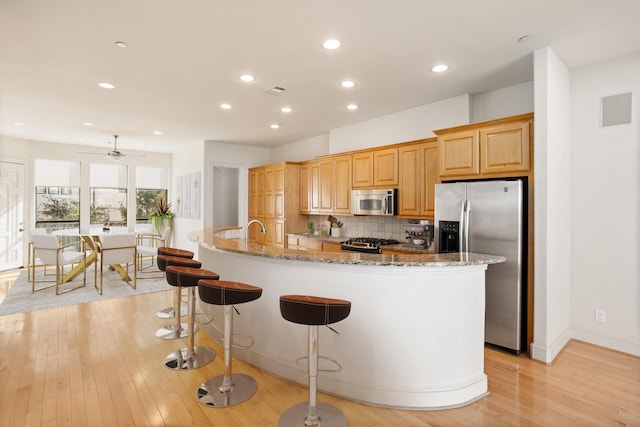 kitchen with backsplash, appliances with stainless steel finishes, a kitchen island with sink, and light stone counters