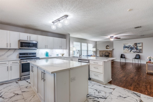 kitchen with white cabinets, open floor plan, a center island, a peninsula, and stainless steel appliances