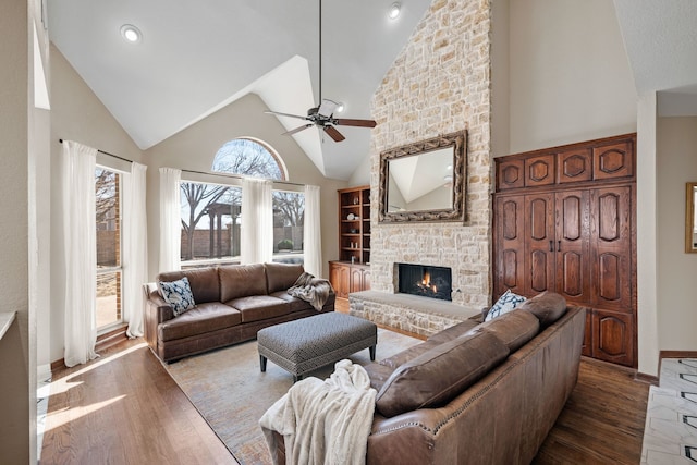 living area with high vaulted ceiling, a fireplace, wood finished floors, a ceiling fan, and baseboards