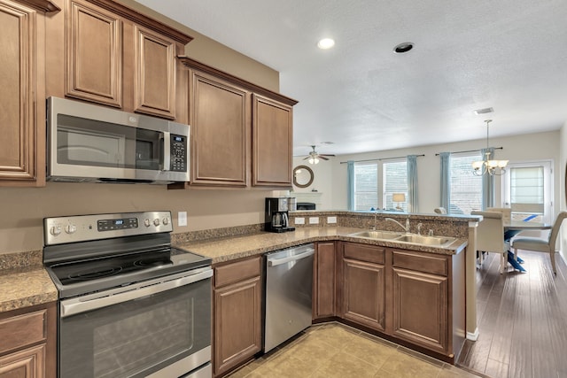 kitchen with appliances with stainless steel finishes, decorative light fixtures, ceiling fan with notable chandelier, sink, and kitchen peninsula