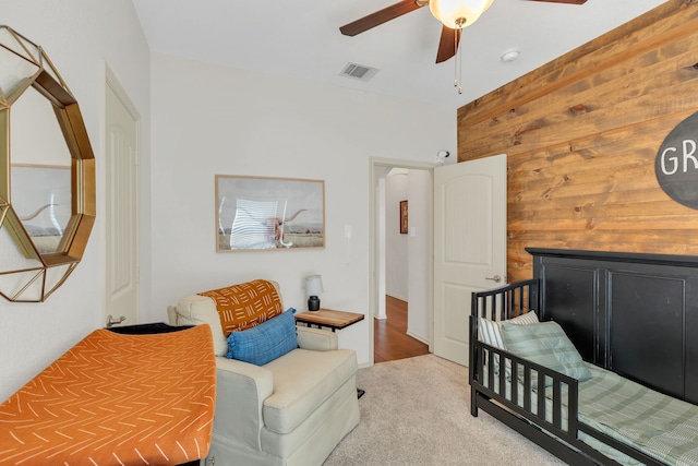 bedroom with ceiling fan, wood walls, and light colored carpet