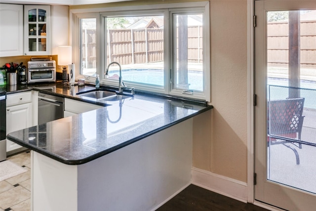 kitchen with white cabinets, dishwasher, glass insert cabinets, a peninsula, and a sink