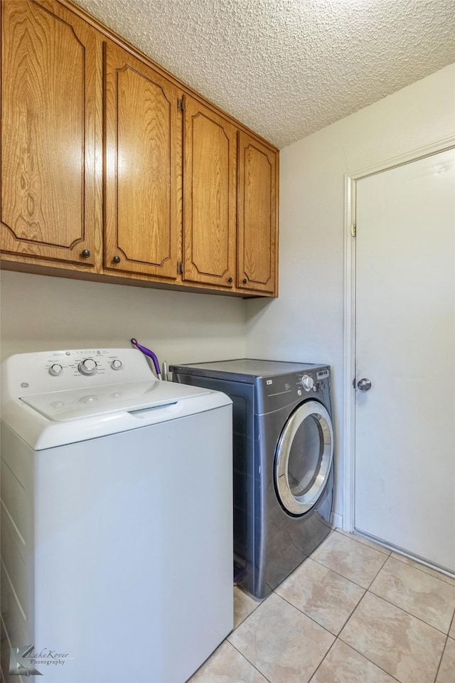 clothes washing area with cabinets, light tile patterned floors, a textured ceiling, and independent washer and dryer