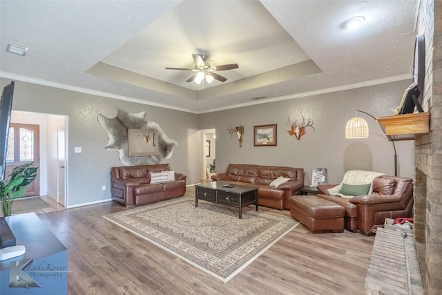 living room with ceiling fan, light wood-type flooring, a tray ceiling, and crown molding