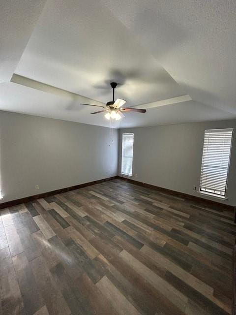 empty room with a tray ceiling, ceiling fan, and dark hardwood / wood-style flooring