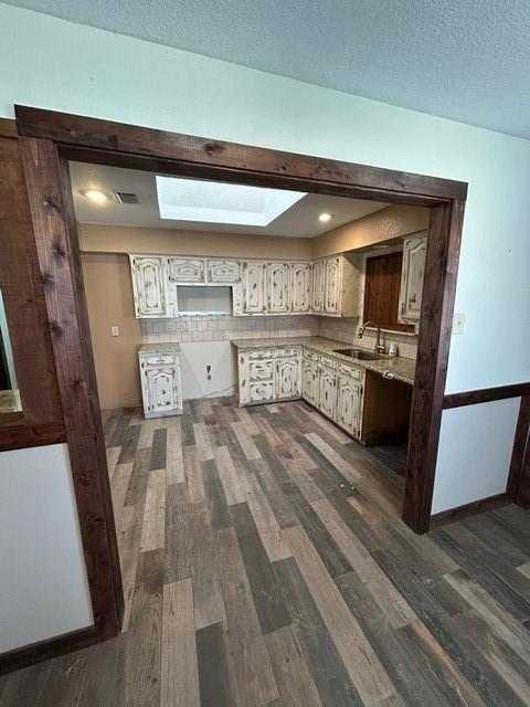 kitchen featuring a textured ceiling, white cabinets, a skylight, dark hardwood / wood-style flooring, and sink