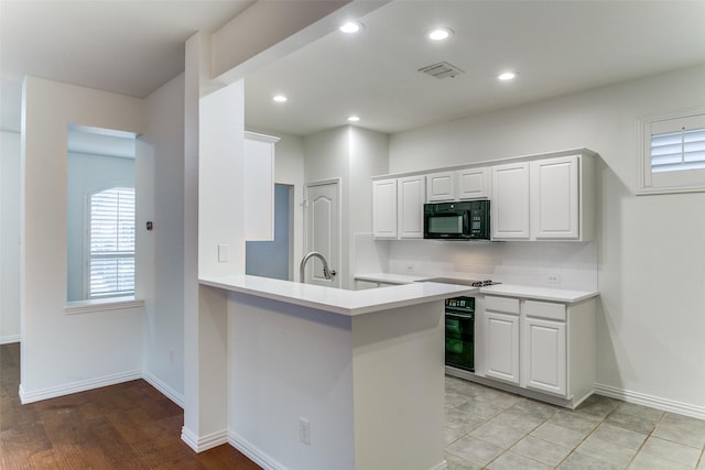 kitchen with kitchen peninsula, tasteful backsplash, black appliances, and white cabinets