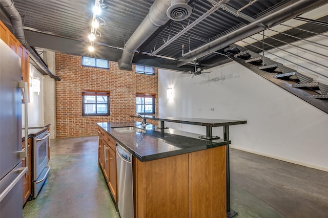 kitchen featuring a center island with sink, brick wall, sink, dark stone counters, and appliances with stainless steel finishes