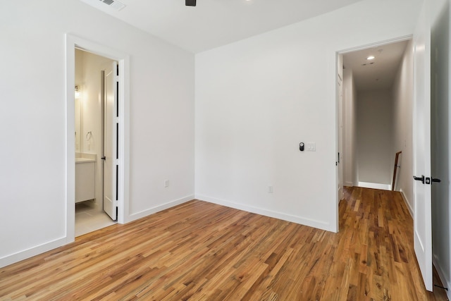 unfurnished bedroom with visible vents, wood finished floors, connected bathroom, and baseboards