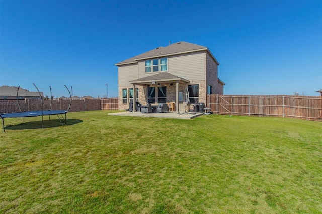 rear view of house featuring a trampoline, brick siding, a lawn, a patio area, and a fenced backyard