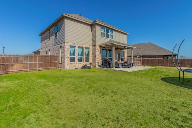 back of property featuring a fenced backyard, brick siding, a yard, a trampoline, and a patio area