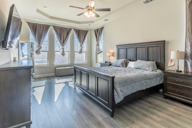 bedroom with baseboards, visible vents, ceiling fan, wood finished floors, and a tray ceiling