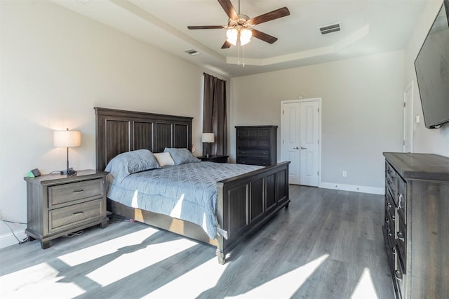 bedroom with a tray ceiling, wood finished floors, visible vents, and baseboards