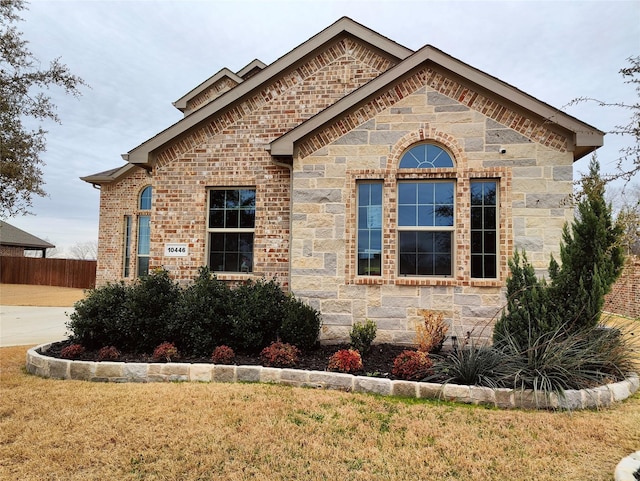 view of front of property featuring stone siding, fence, a front lawn, and brick siding